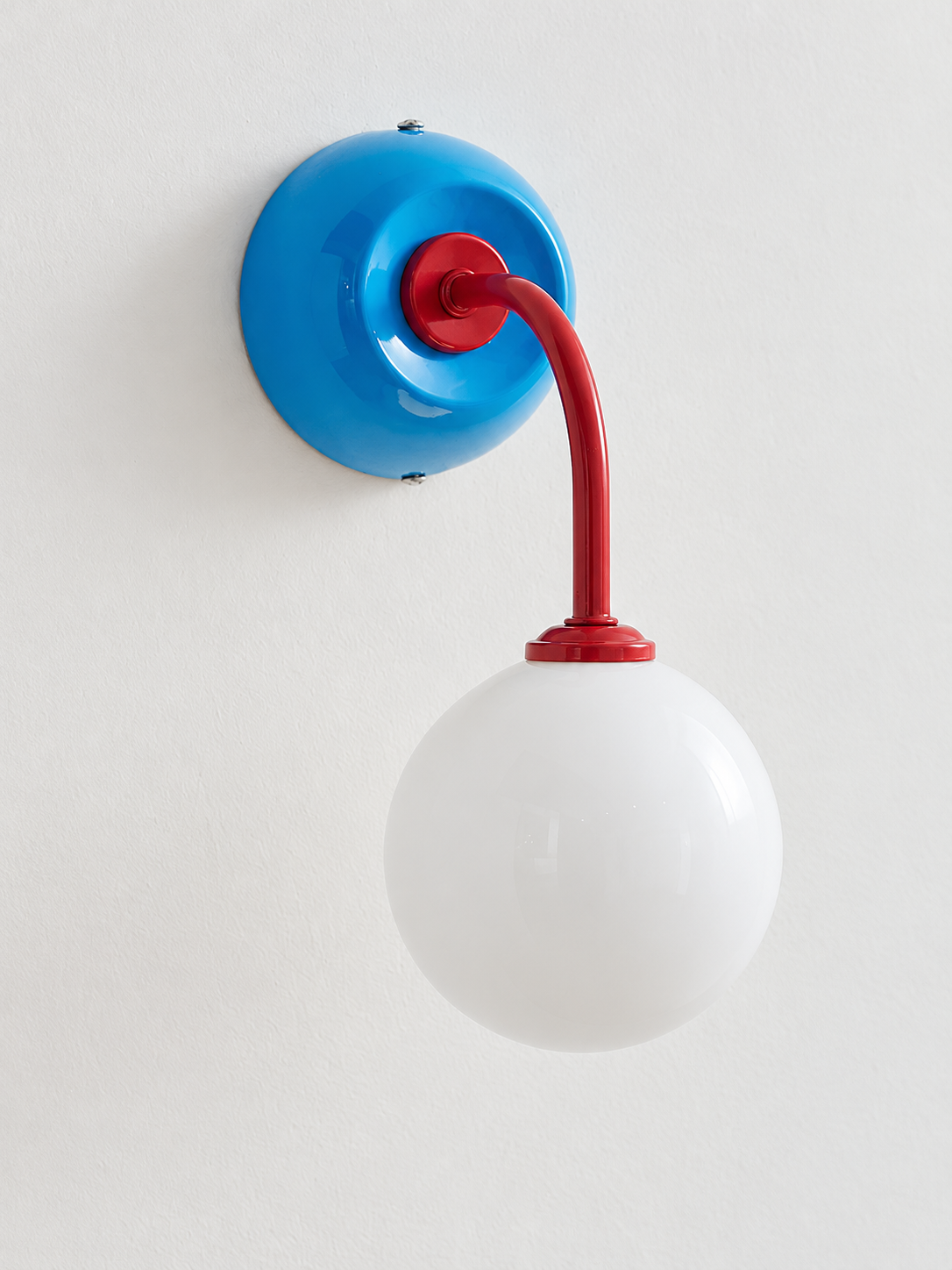 Blue + Red wall sconce with curved red arm and white glass globe, shown unlit, product view