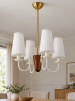 Scroll-arm chandelier with 4 white pleated fabric shades, shown unlit, daylight dining-room setting