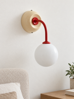 Ivory + Red wall sconce with curved red arm and white glass globe, shown unlit, daylight bedside setting