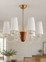 Scroll-arm chandelier with 6 white pleated fabric shades, shown unlit, daylight dining-room setting