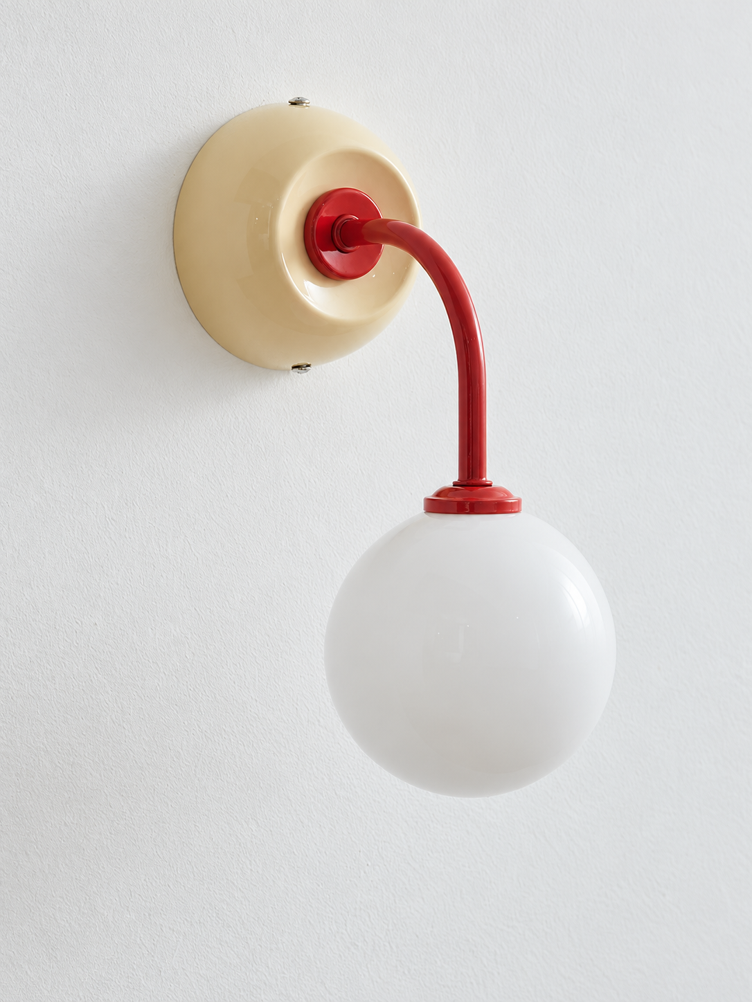 Ivory + Red wall sconce with curved red arm and white glass globe, shown unlit, complete-fixture detail view
