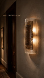 Warm light passing through the Cinder Veil ribbed glass wall sconce