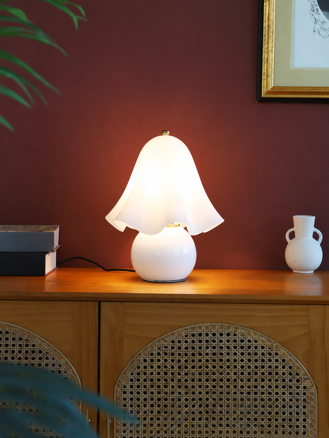 White draped glass table lamp illuminated on a wooden cabinet