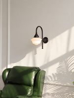 Black curved arm wall light with white bowl shade above a green armchair