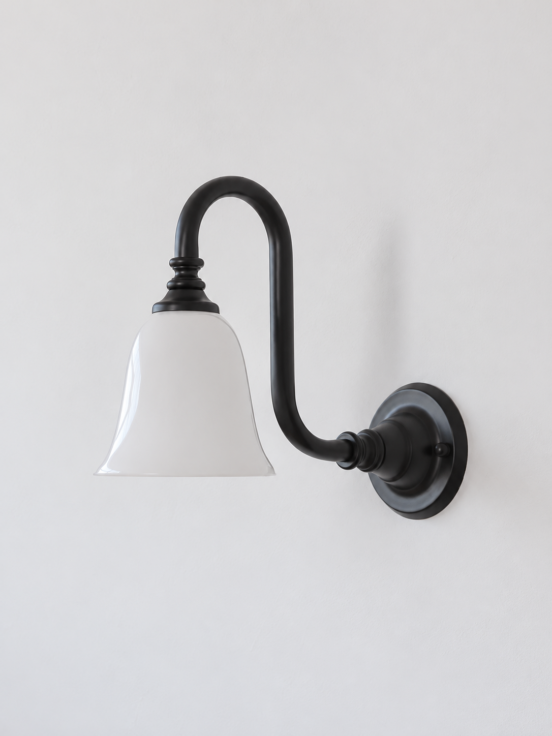 Black bent arm wall sconce with a white glass shade, shown unlit