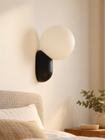 Black capsule and opal globe wall light beside a bed