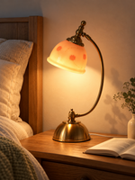 Blush Bloom Arc 220V table lamp glowing warmly beside linen bedding on an oak nightstand