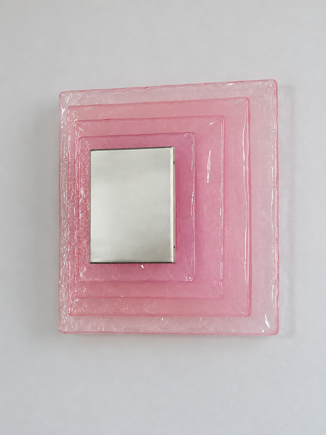 Large wall sconce with pink textured glass and white acrylic insert behind a brushed-metal cover, shown switched off in daylight