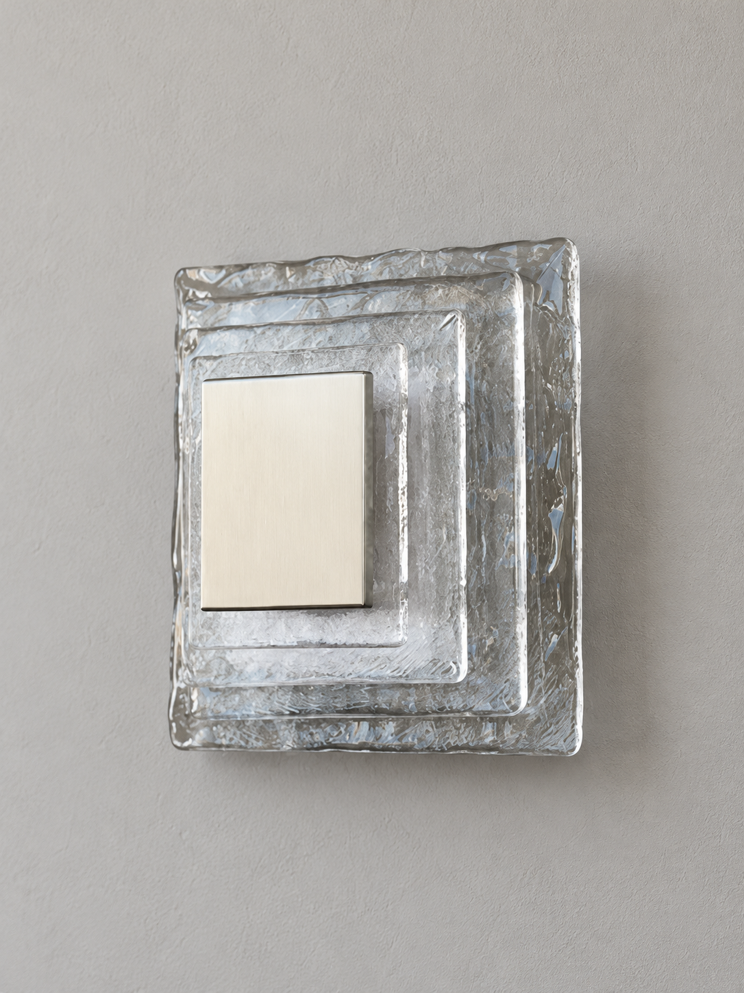 Small wall sconce with clear textured glass and white acrylic insert behind a brushed-metal cover, shown switched off in daylight