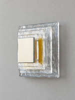 Small wall sconce with clear textured glass and yellow acrylic insert behind a brushed-metal cover, shown switched off in daylight
