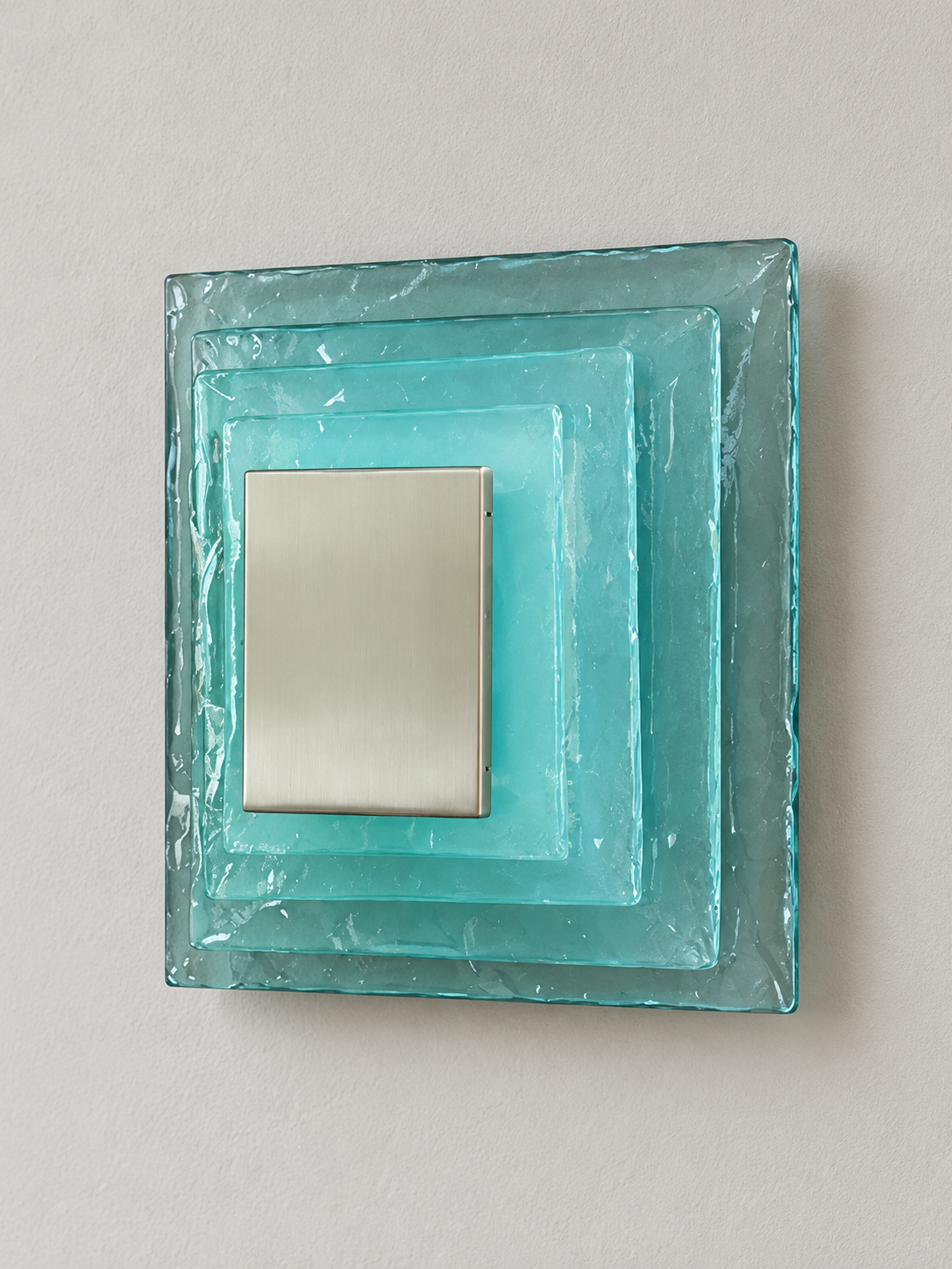 Large wall sconce with blue textured glass and white acrylic insert behind a brushed-metal cover, shown switched off in daylight