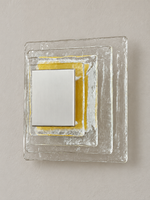 Large wall sconce with clear textured glass and yellow acrylic insert behind a brushed-metal cover, shown switched off in daylight