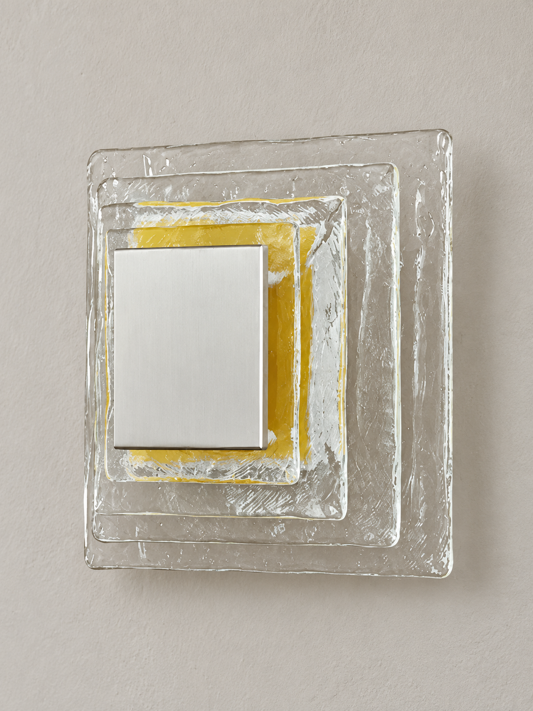 Large wall sconce with clear textured glass and yellow acrylic insert behind a brushed-metal cover, shown switched off in daylight