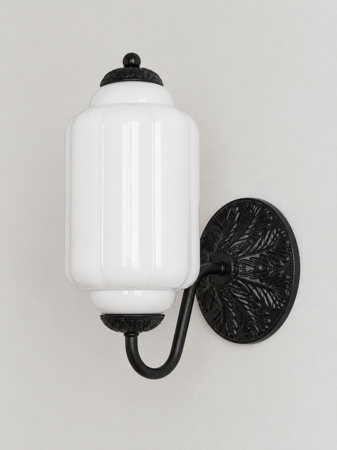 White ribbed glass wall sconce with black U-arm and ornate round medallion backplate, shown switched off