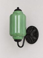 Green ribbed glass wall sconce with black U-arm and ornate round medallion backplate, shown switched off