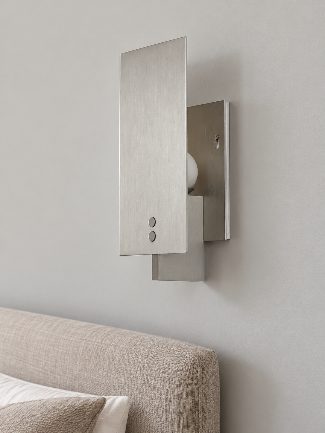 Panel Glow wall sconce in Aluminum Tone, unlit beside a linen headboard