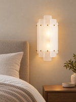 Tiered glass wall sconce beside a linen bed