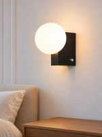 Black opal-globe wall sconce above a bedside table
