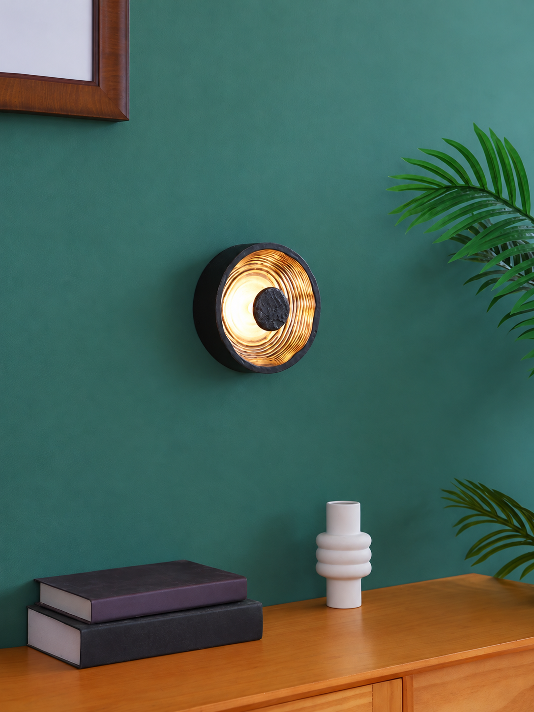 Black and gold ripple disc wall light in a green-wall interior