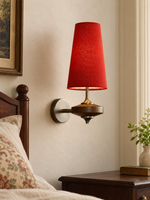 Red tapered fabric wall sconce with brown wood and metal body in a bedroom