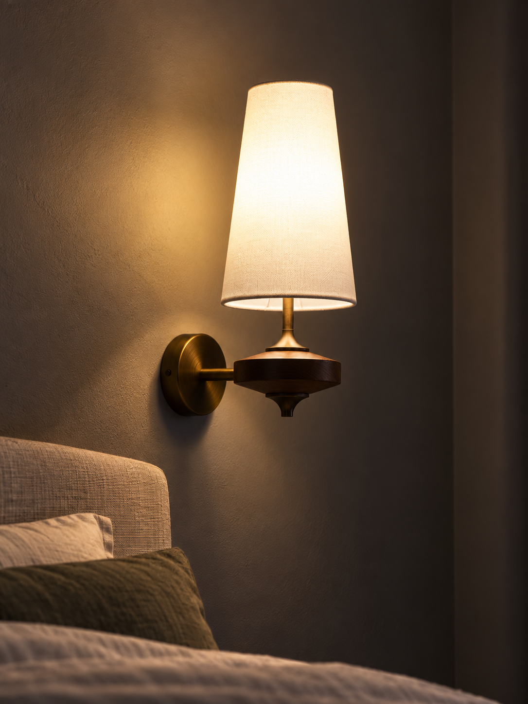 Illuminated white fabric wood wall sconce beside a bed
