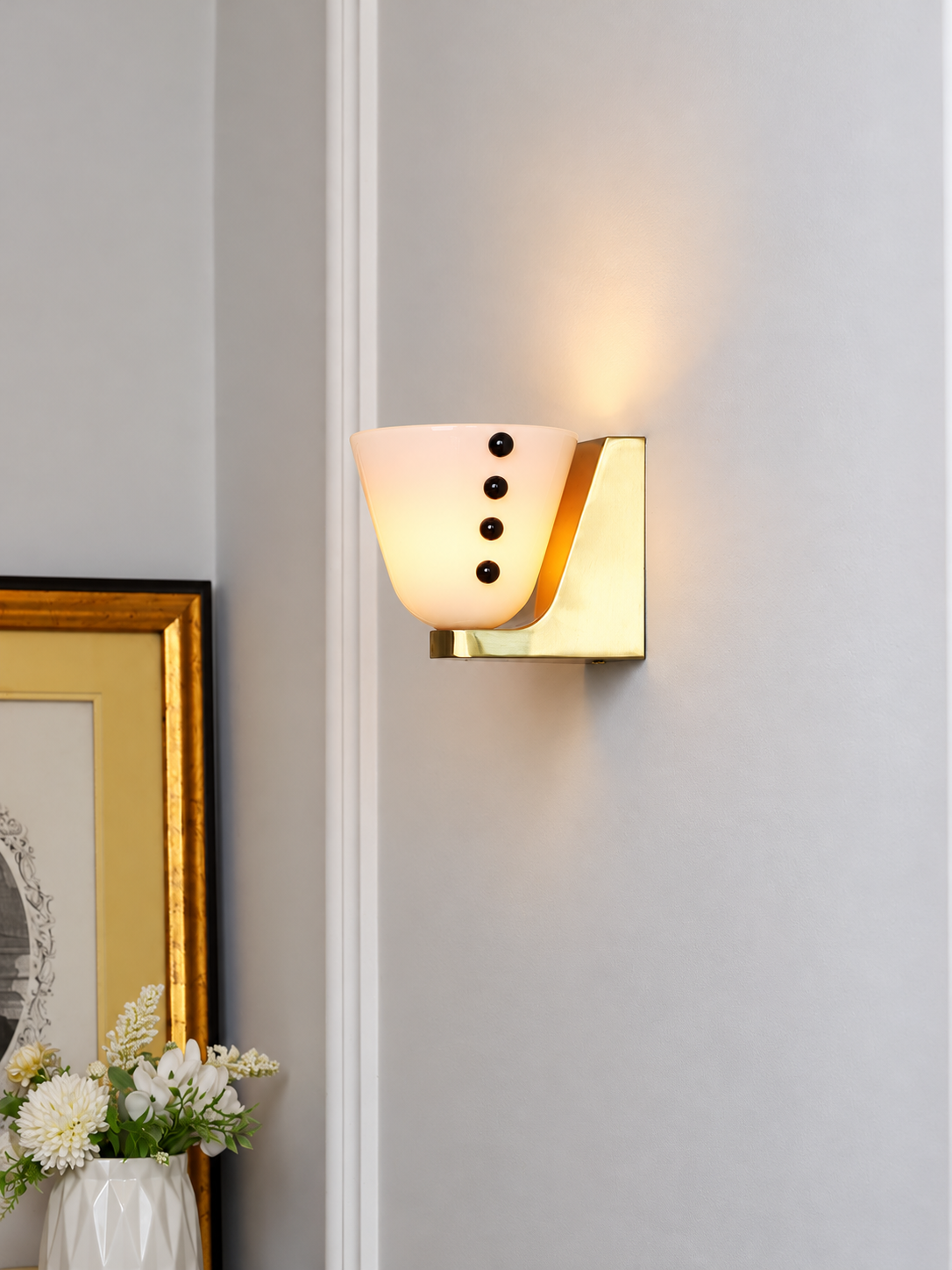 White glass cup wall light next to framed art and flowers