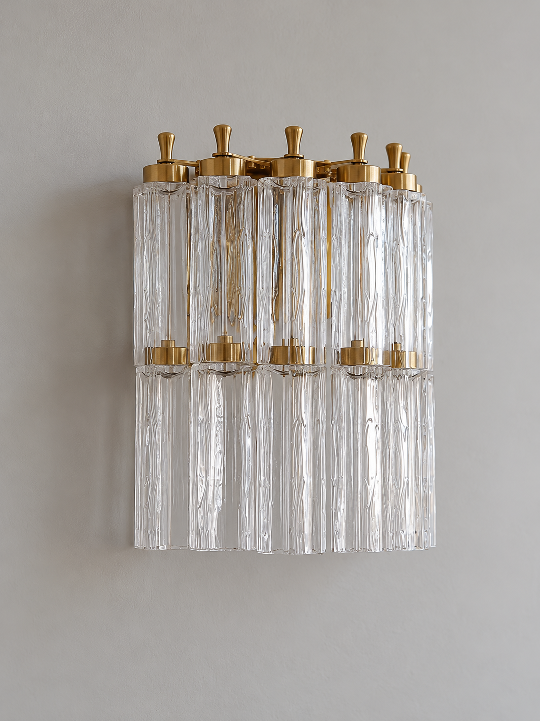 Clear fluted-glass wall sconce shown unlit, with two rows of glass columns and copper-tone finials
