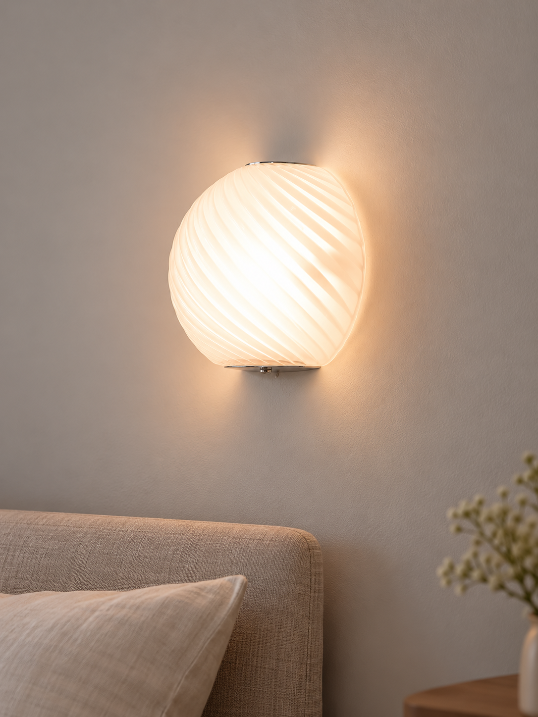 Spiral glass wall sconce in White opal glass glowing beside a linen headboard