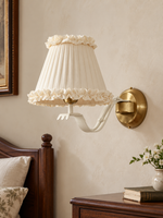 Ruffle Arm Fabric Wall Sconce with ivory ruffled shade and copper-tone backplate, switched off in a bedroom
