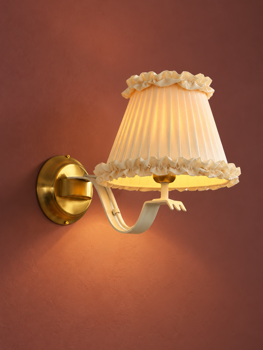Ivory Ruffled Shade wall sconce illuminated, showing pleated fabric and curved ivory arm